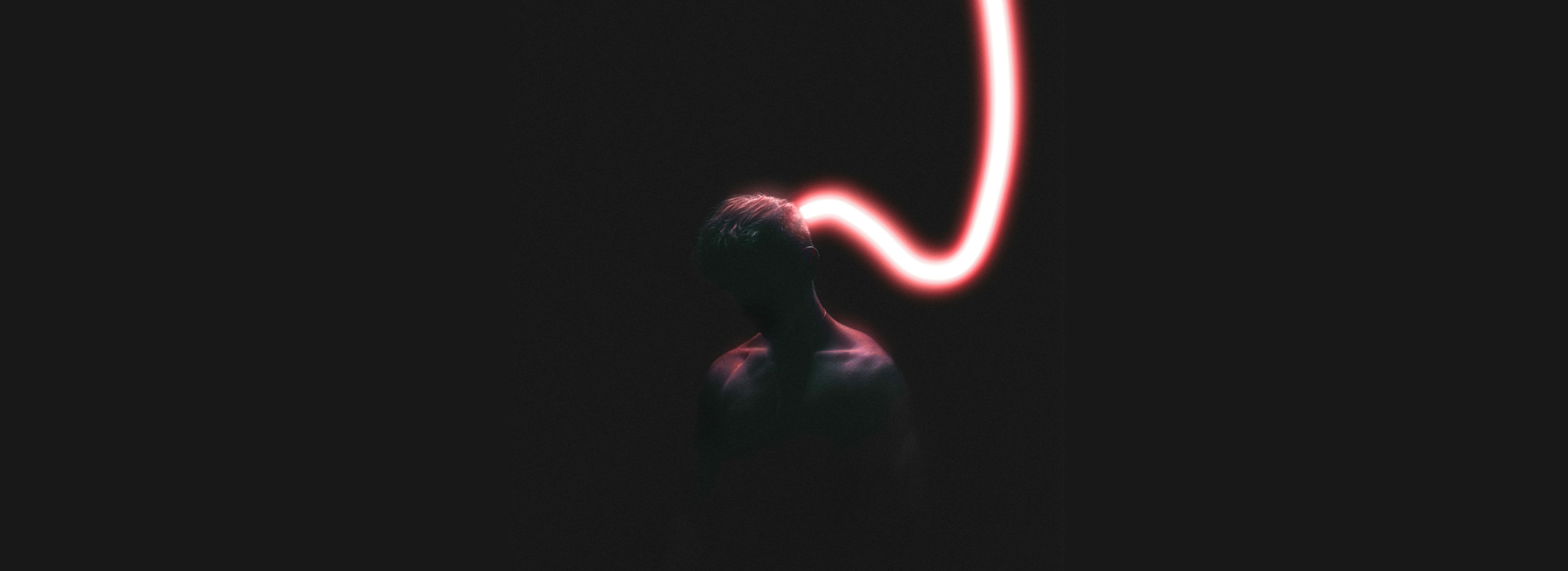 Σιλουέτα ανθρώπου σε σκοτάδι με κόκκινη φωτεινή γραμμή πίσω από το κεφάλι, σύμβολο της σχέσης ανθρώπινης σκέψης και AI.